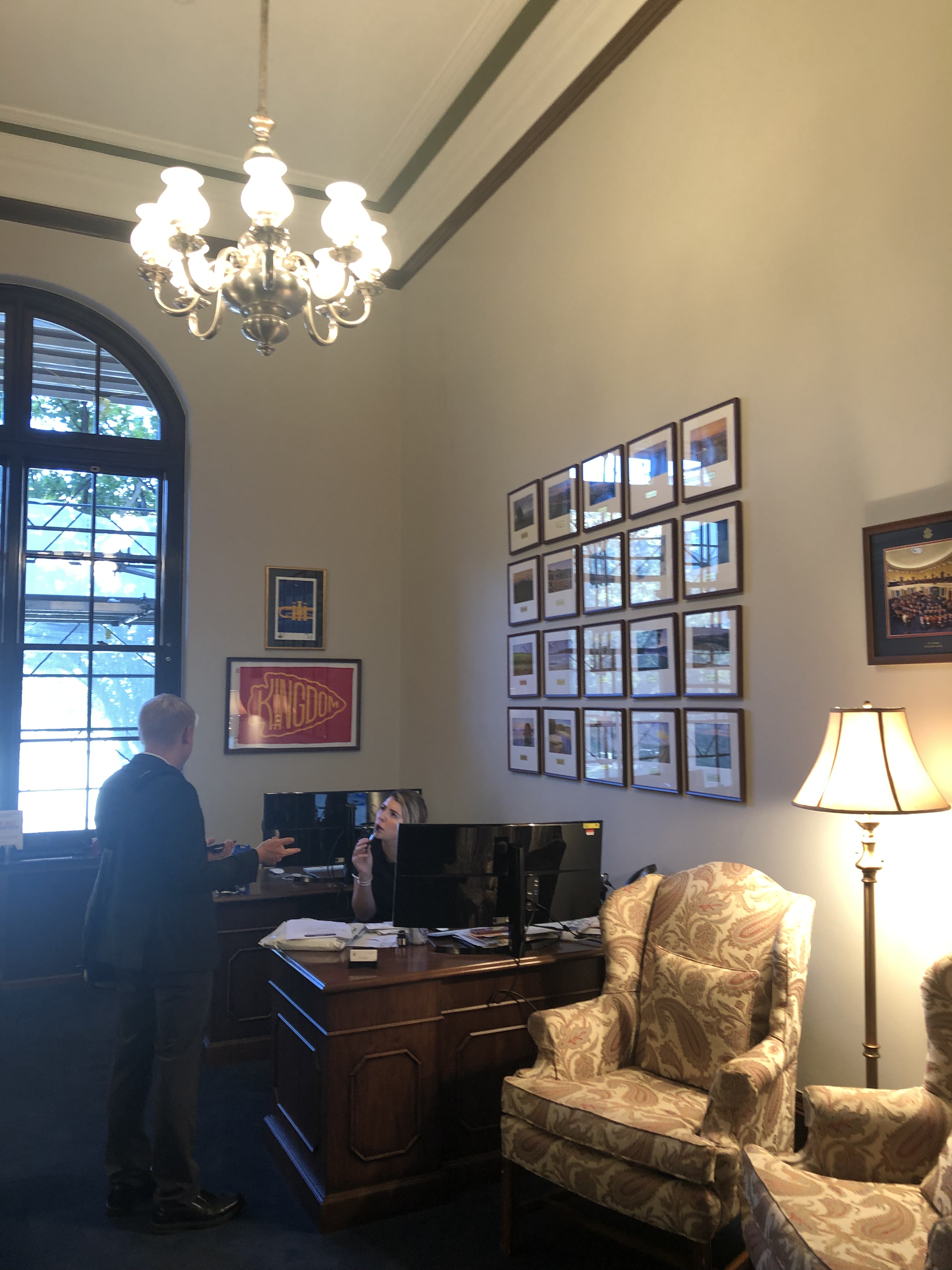 Picture of an office with two arm chaos a man and woman conversing in background . Framed picture of St. Louis Blies and KC chiefs posters