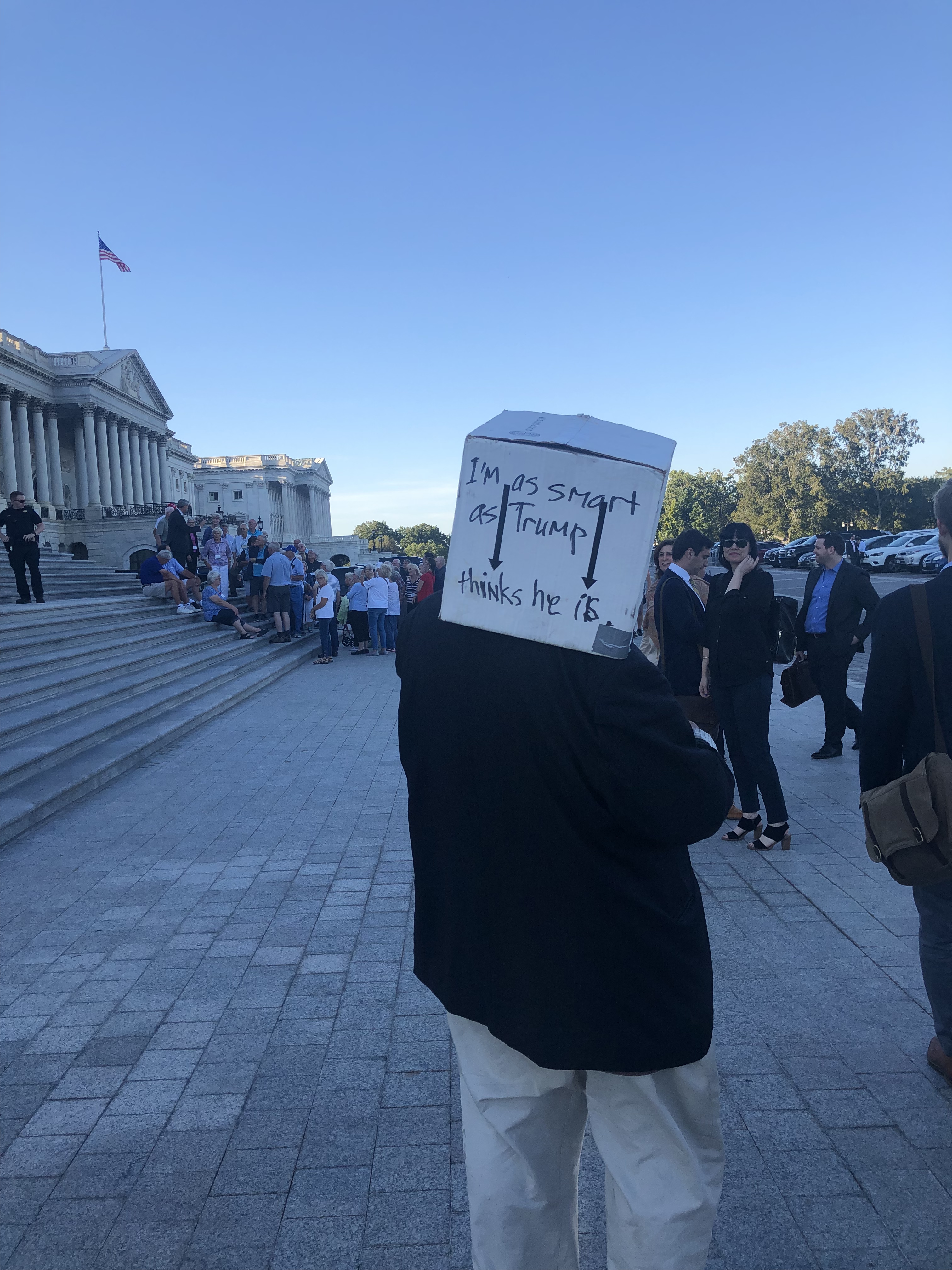 Man in a suit wearing a box on his head that says “I’m as same as Trump thinks he is.”